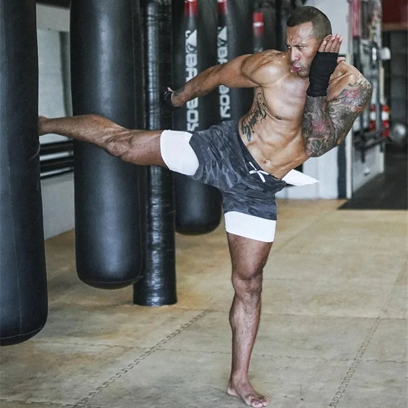 man kicking a heavy bag with grey camo shorts 